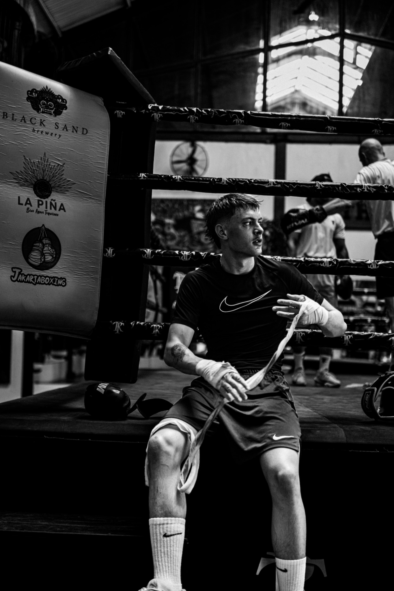 Andri Casutt seated at the ring, wrapping his hands as training continues behind him.